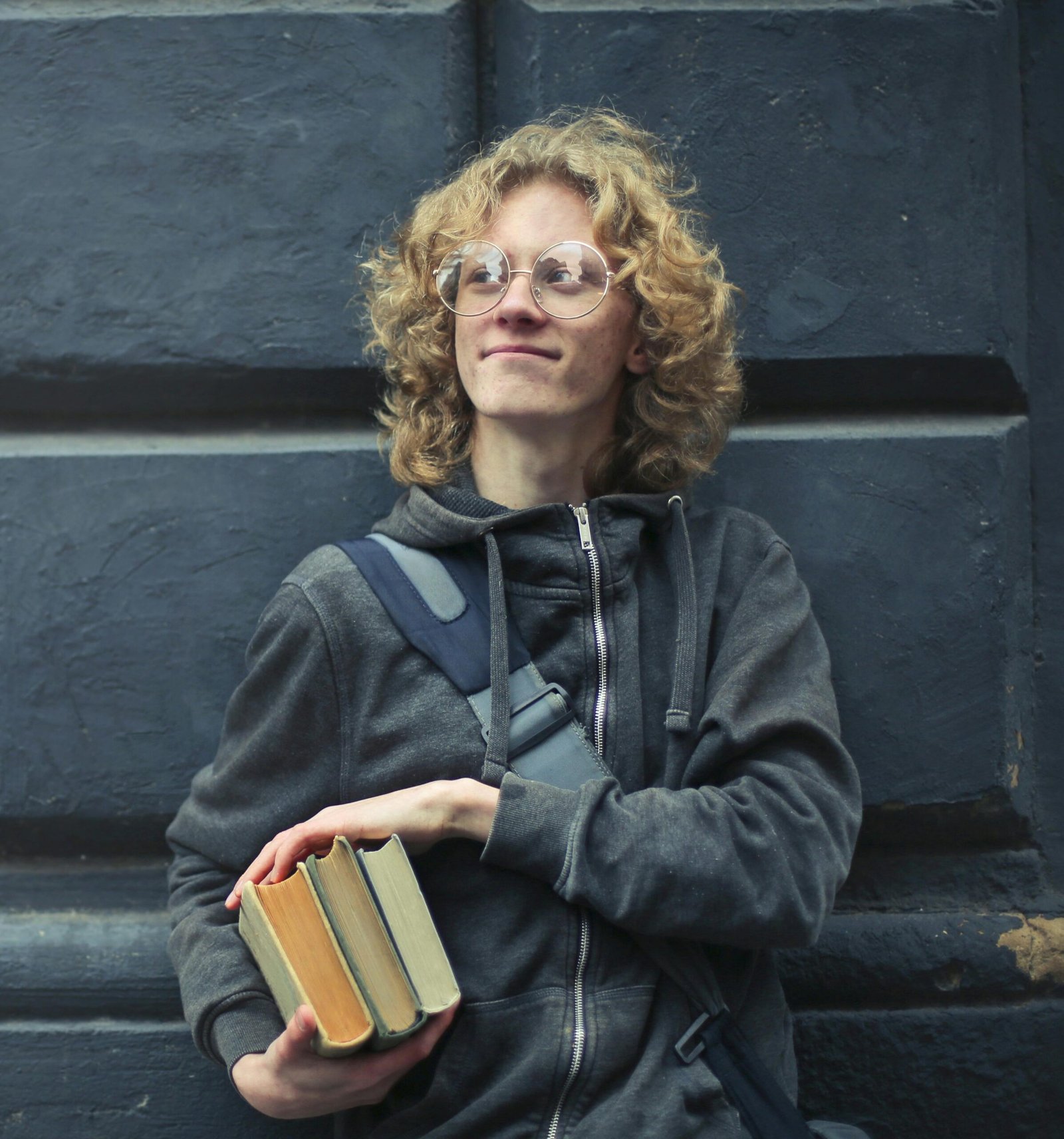 A student carrying books leaning on a wall